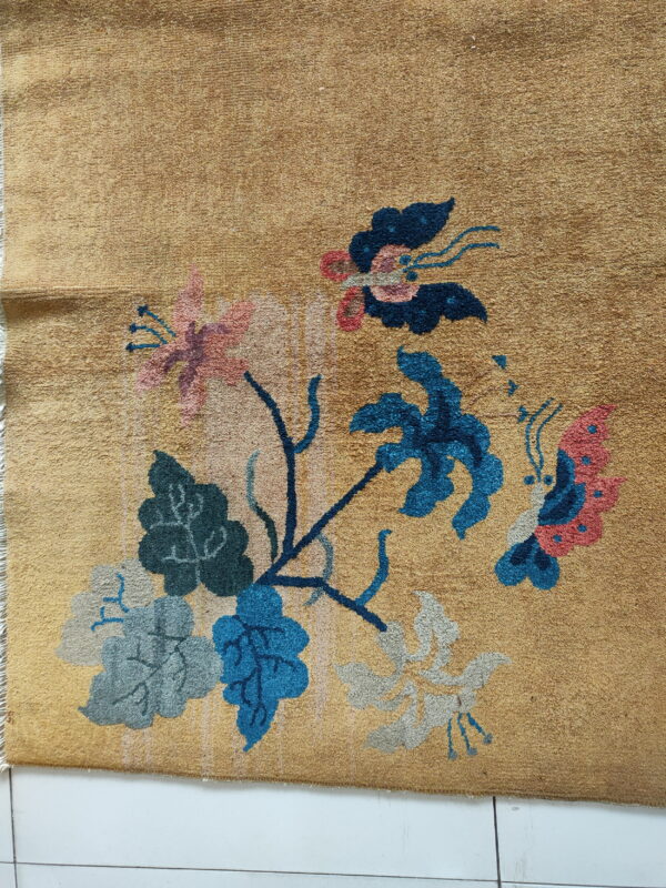 Golden rug displaying a multicolored floral and butterfly design over white square tiles.