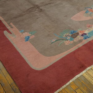 A brown rug with a deep red border displays stylized floral patterns in blue, pink, and green on wood planks.