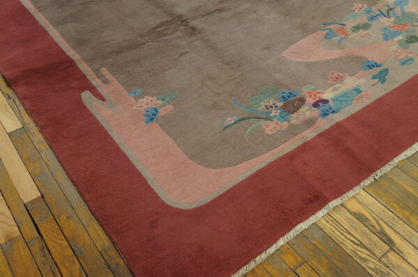 A brown rug with a deep red border displays stylized floral patterns in blue, pink, and green on wood planks.