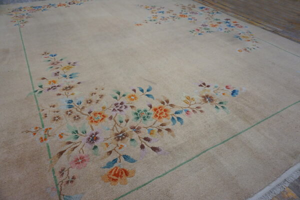 Tan rug with multicolored floral spandrels and a green outline rests on dark wood flooring.