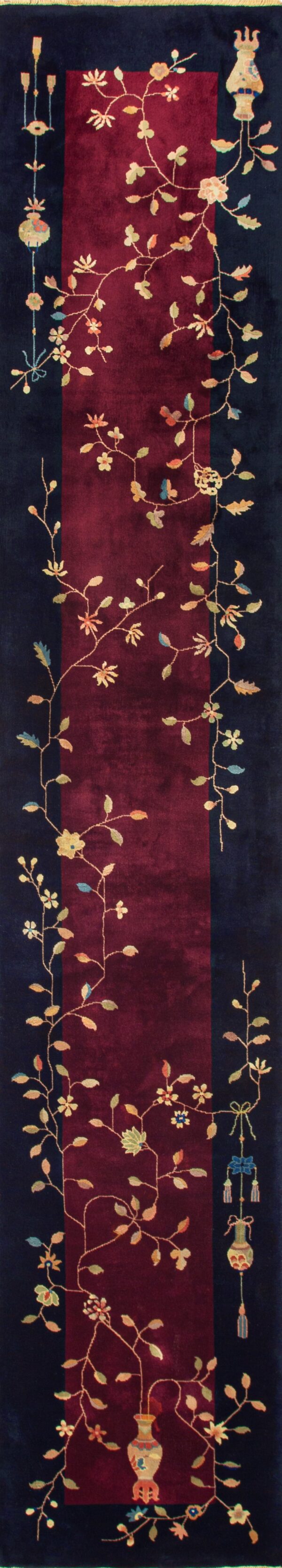Dark runner rug with a burgundy field and scrolling floral pattern lying on light wood planks.