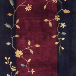 Dark runner rug with a burgundy field and scrolling floral pattern lying on light wood planks.