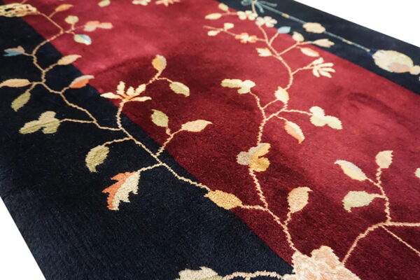Detailed view of a high-pile rug with maroon and black fields and delicate light-colored floral vines.