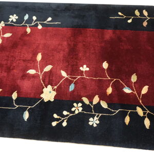 Red field rug bordered by dark stripes featuring an intricate light-colored floral and vine pattern.