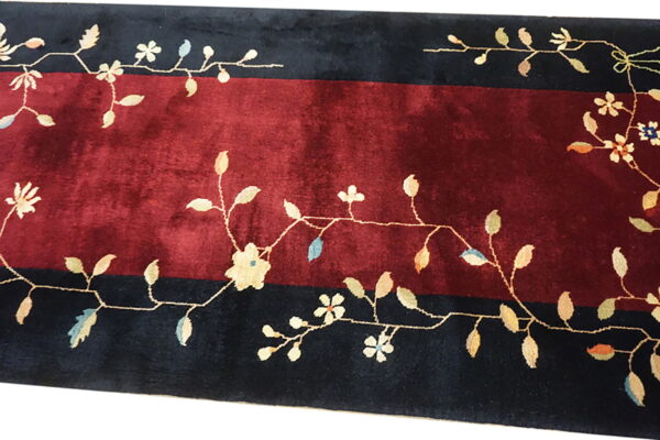 Red field rug bordered by dark stripes featuring an intricate light-colored floral and vine pattern.