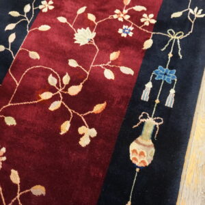 Plush burgundy rug with navy borders featuring delicate floral vines and decorative motifs on worn wood floors.