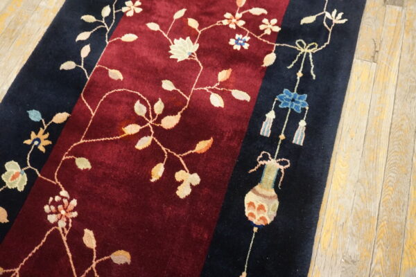 Plush burgundy rug with navy borders featuring delicate floral vines and decorative motifs on worn wood floors.