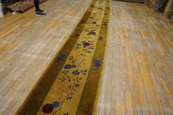 A golden yellow runner with blue and maroon floral patterns lies on distressed wood plank flooring.