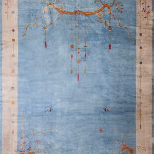 Light blue rug with wide tan border decorated with stylized hanging lanterns and floral vases.