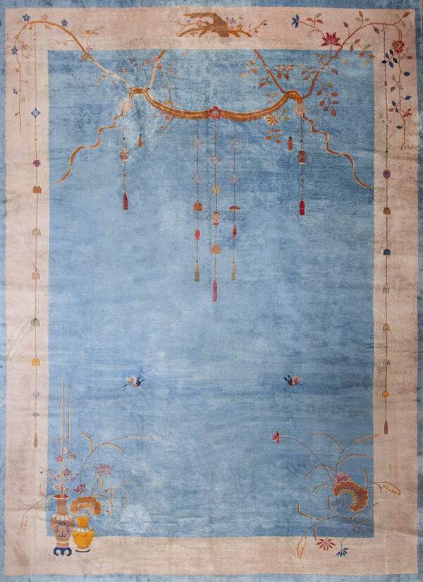 Light blue rug with wide tan border decorated with stylized hanging lanterns and floral vases.