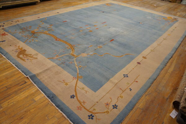 Large blue rug with a golden stylized tree pattern and a thick beige border lies on hardwood floors.
