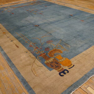 Large blue rug with a beige border and vase motifs rests on rustic hardwood flooring.