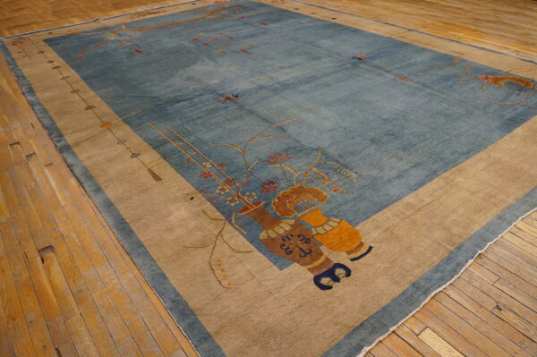 Large blue rug with a beige border and vase motifs rests on rustic hardwood flooring.