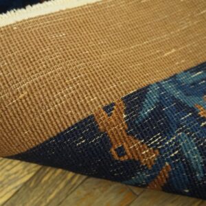 Close-up of a rolled rug showing the textured tan backing and the patterned navy, blue, and rust pile.