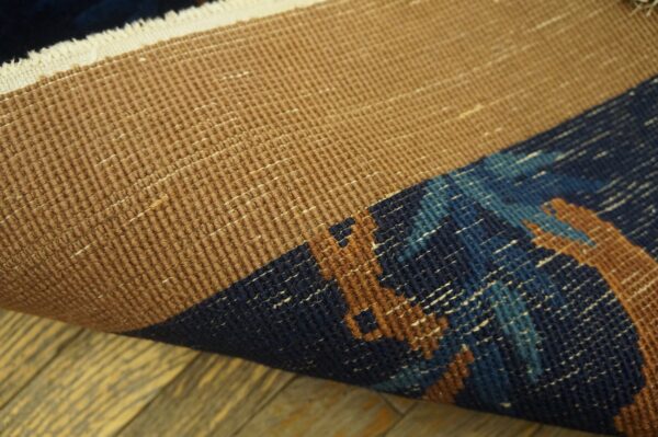 Close-up of a rolled rug showing the textured tan backing and the patterned navy, blue, and rust pile.