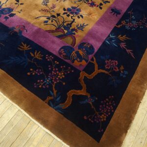 Gold field rug with purple and navy floral borders rests on a distressed pale wood floor.
