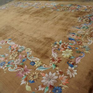 Golden brown area rug with a multicolor pastel floral border lies on dark wood floors.
