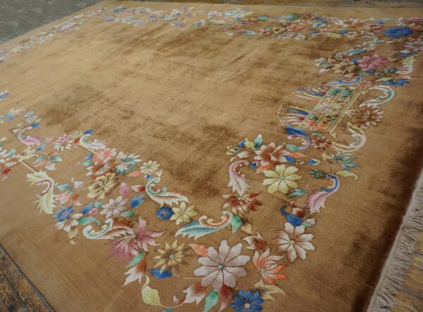 Golden brown area rug with a multicolor pastel floral border lies on dark wood floors.