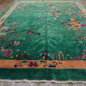 Emerald green area rug with high-luster pile, colorful ornate floral motifs, and terracotta borders on wood flooring.