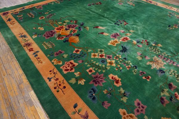 High-pile green rug with multicolor floral motifs and an orange border rests on a worn wood floor.