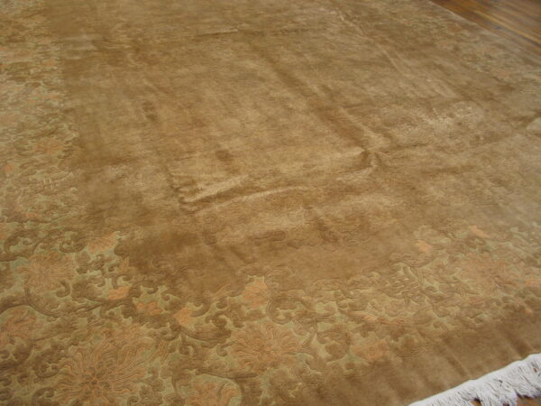 Brown velvety rug with a detailed floral border in tan and sage green, featuring white fringe on hardwood.