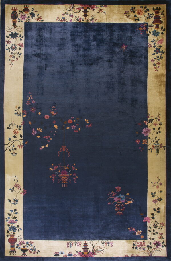 Dark blue rug featuring a sheen and a wide beige border decorated with intricate flowering branches and vases.