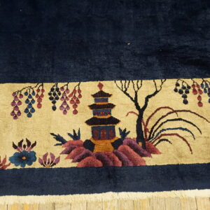 High-pile navy rug border with a beige scenic pattern of a pagoda, flowers, and foliage resting on wood.