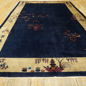 Dark blue rug featuring colorful traditional motifs and a wide golden-tan border, placed on wood plank flooring.