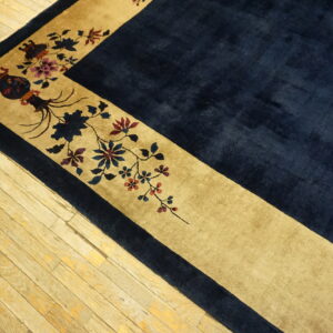 Navy high-pile rug corner featuring a tan border with detailed floral and ornamental patterns on wood floors.