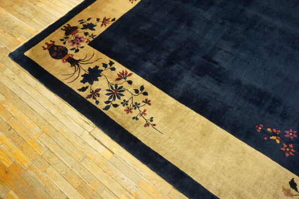 Navy high-pile rug corner featuring a tan border with detailed floral and ornamental patterns on wood floors.
