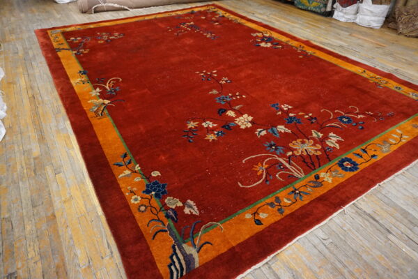 Ornate red rug with a wide orange border and colorful floral motifs displayed on distressed wood planks.