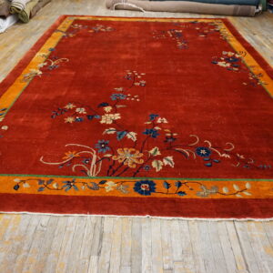 Red rug featuring blue and beige floral vines and a wide orange border on distressed wooden plank flooring.