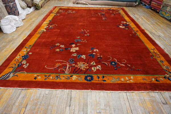 Red rug featuring blue and beige floral vines and a wide orange border on distressed wooden plank flooring.