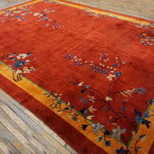 A red rug featuring scattered blue and cream florals, bordered by wide yellow and rust bands, resting on wood.