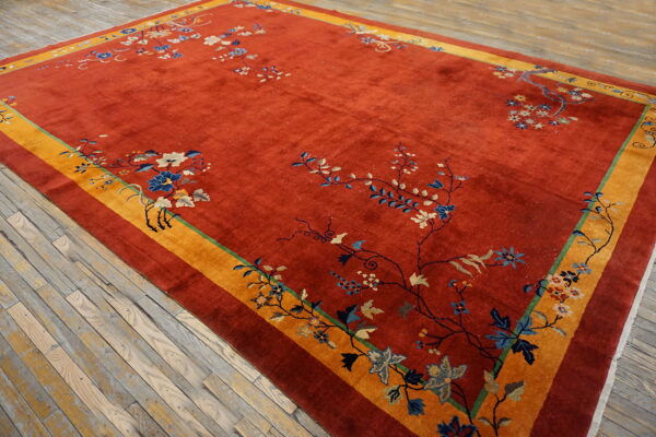 A red rug featuring scattered blue and cream florals, bordered by wide yellow and rust bands, resting on wood.