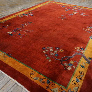 High-pile rust rug with sparse blue floral accents and a wide mustard border on distressed wood.