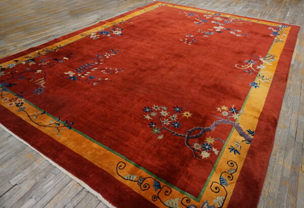 High-pile rust rug with sparse blue floral accents and a wide mustard border on distressed wood.