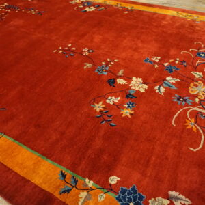 A deep red, high-pile rug displays delicate blue and cream floral vines surrounded by a bright orange border.