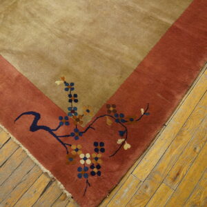 Plush tan rug corner with a rust border and floral design rests on worn yellow wooden planks.