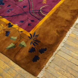 Plush rug with a purple field, rusty brown border, and floral pattern rests on worn wood flooring.