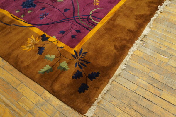 Plush rug with a purple field, rusty brown border, and floral pattern rests on worn wood flooring.