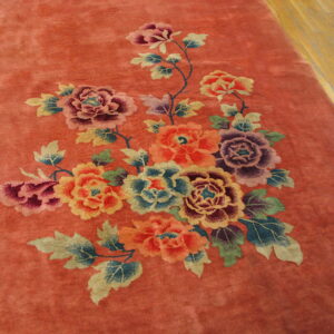 Rust colored rug with a large multicolored floral motif resting on light wood flooring.