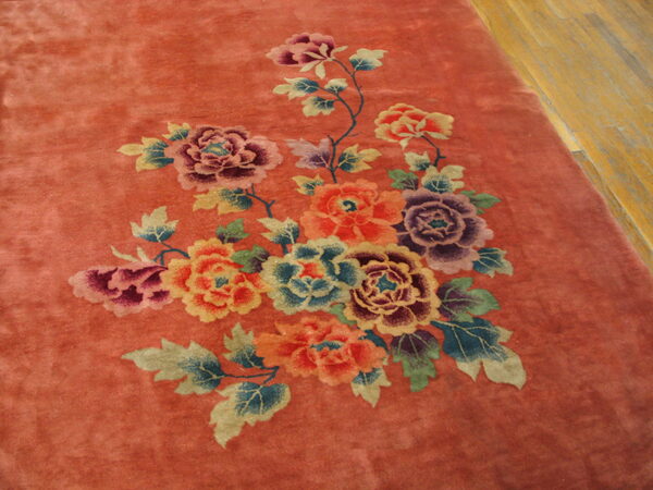 Rust colored rug with a large multicolored floral motif resting on light wood flooring.