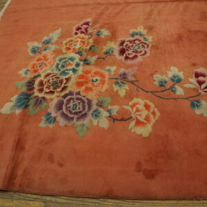 Coral rug with colorful rose, lavender, and blue floral motifs laid on light brown hardwood flooring.
