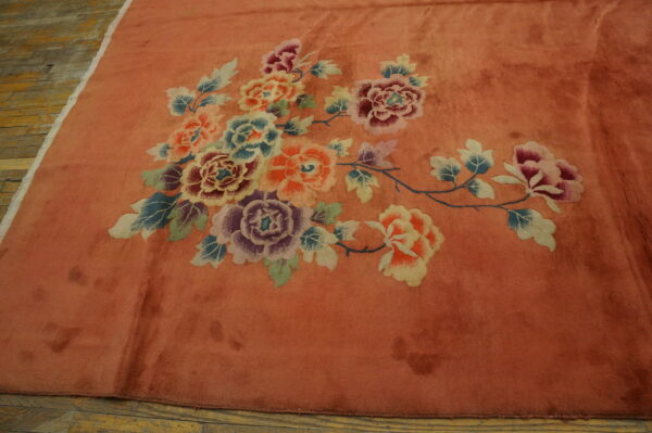 Coral rug with colorful rose, lavender, and blue floral motifs laid on light brown hardwood flooring.