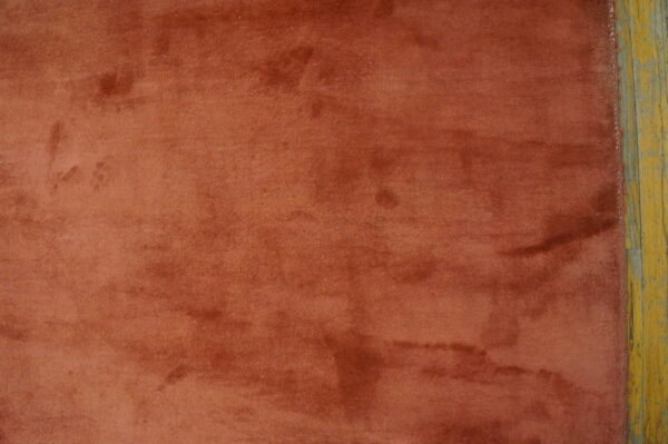 Low-pile rust rug showing color variation and shading next to distressed yellow painted hardwood floor.