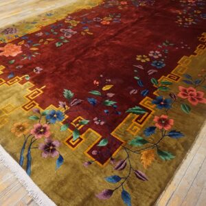 Maroon rug featuring multicolored florals, an olive geometric border, and a visible high pile on wood flooring.