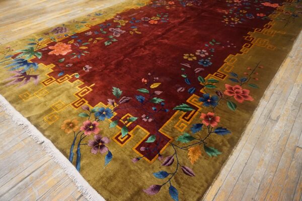 Maroon rug featuring multicolored florals, an olive geometric border, and a visible high pile on wood flooring.