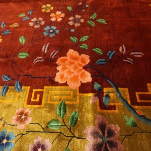 Plush rug detail showing multicolored blossoms on rust and ochre fields with a geometric border design.