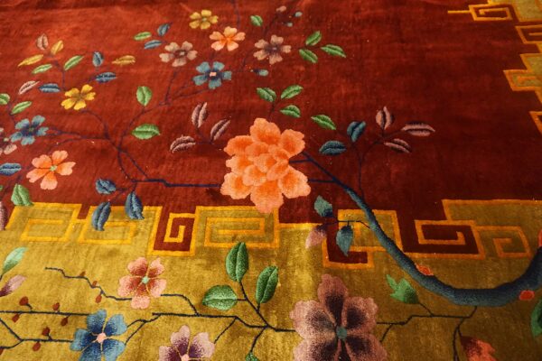 Plush rug detail showing multicolored blossoms on rust and ochre fields with a geometric border design.